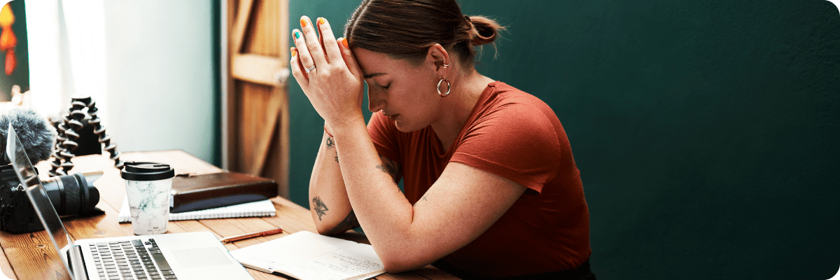 Stressed small business owner at a desk with their head in their hands, surrounded by work materials.