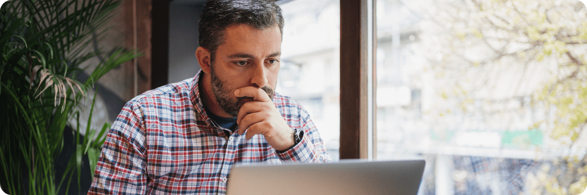 A business owner writing goals in a notebook while using a laptop to research digital marketing strategies.