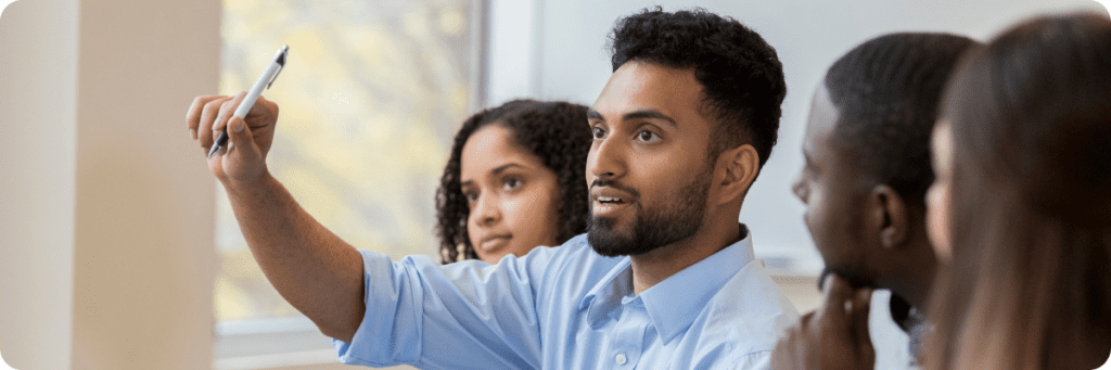 A diverse team collaborating in a meeting, with a man pointing towards the front to share an idea, symbolising teamwork in digital marketing strategy.