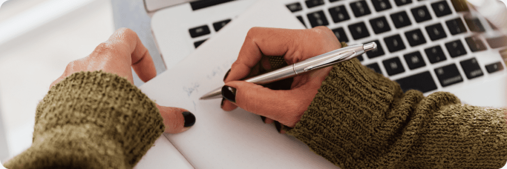 Hand writing in a notebook with a laptop in the background, representing thoughtful planning for business owners.