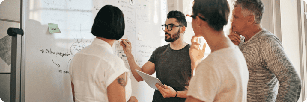 A group of professionals gathered around a whiteboard, brainstorming and strategising for a marketing project, showcasing collaborative problem-solving.