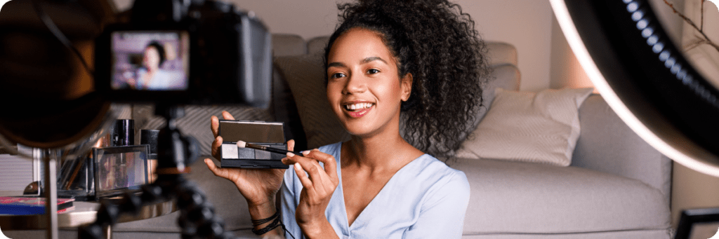 A beauty influencer smiling while applying makeup in front of a camera with professional lighting before the TikTok US Ban