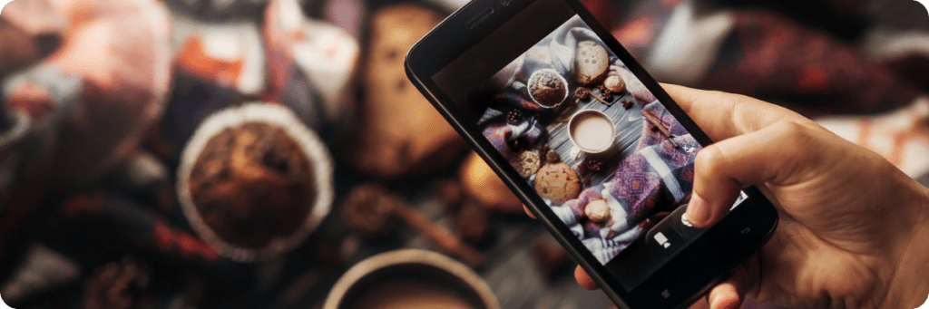 Smartphone capturing a flat lay of a cosy coffee setup with muffins, a cup of tea, and a blanket, showcasing creative content photography for social media like Instagram.