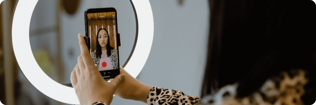 Person recording a video using a ring light and smartphone, illustrating professional short-form video content creation for social media like TikTok and Instagram.